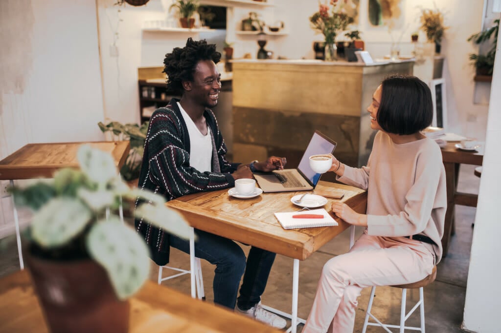 Two employees smile while drinking coffee and working